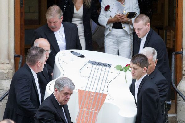 A giant, 12 ft guitar-shaped coffin, followed by his widow June Graham (white suit), is carried out of St Andrew's United Reformed Church at the funeral of musician John Graham