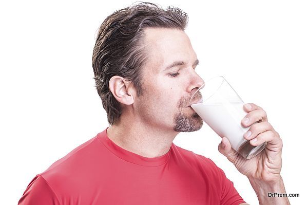 Portrait of handsome muscular Caucasian man with goatee wearing red athletic shirt drinking glass of milk on white background